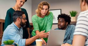 Equipe de desenvolvimento com homens e mulheres discutem a análise da plataforma low-code Mendix com um computador sobre a mesa.