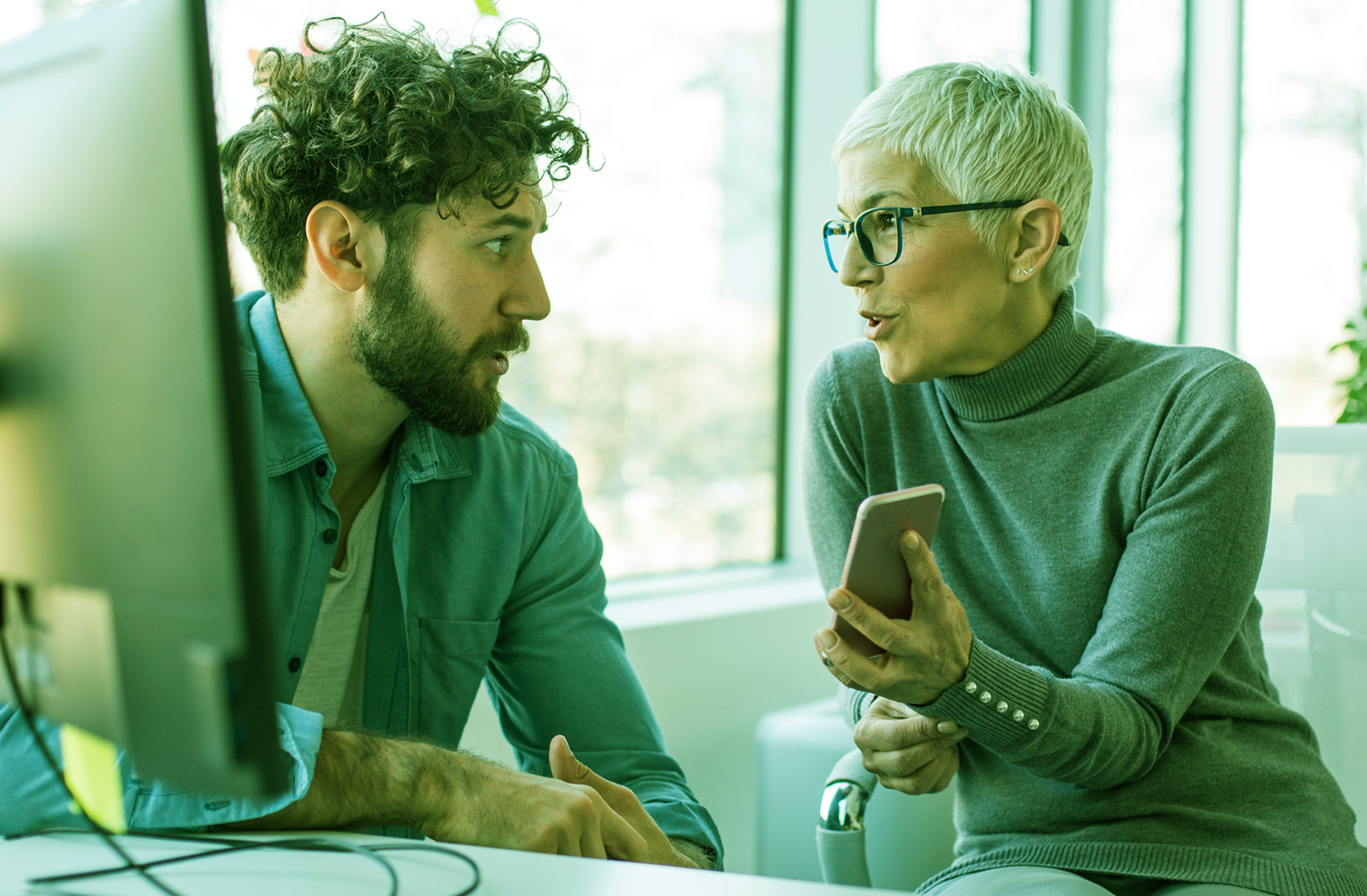 homem ruivo de cabelo enrolado e camisa verde conversando com uma mulher com smartphone na mão, de cabelo curto, branco e blusa verde, discutindo sobre qualidade de software